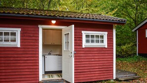 A red wooden cabin with a white door, a small kitchen area, and a window.