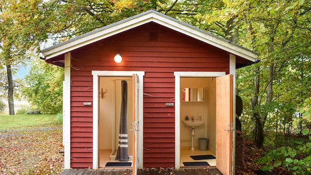 A small, red wooden cabin with two doors, one leading to a shower and the other to a bathroom.