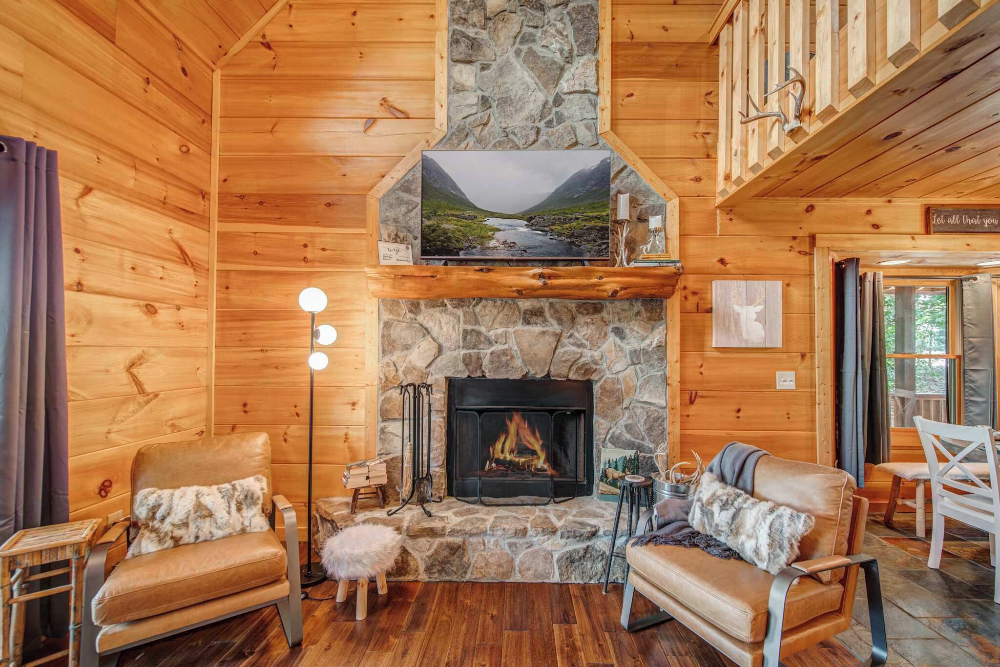 L’intérieur chaleureux d’un chalet avec une cheminée en pierre, des murs en bois et un téléviseur fixé au-dessus.