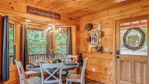 Interior de una cabaña de madera con una mesa de comedor para cuatro personas, una araña y una puerta decorada con un adorno.