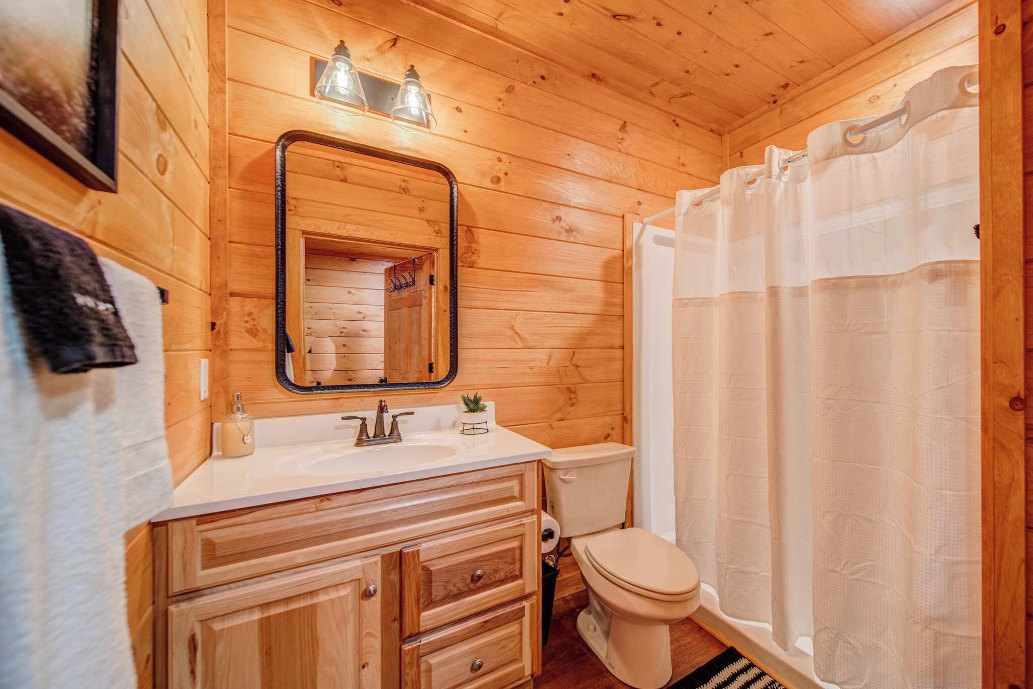 Une salle de bain rustique, aménagée dans une cabane en bois, avec un lavabo, un miroir, des toilettes et un rideau de douche.