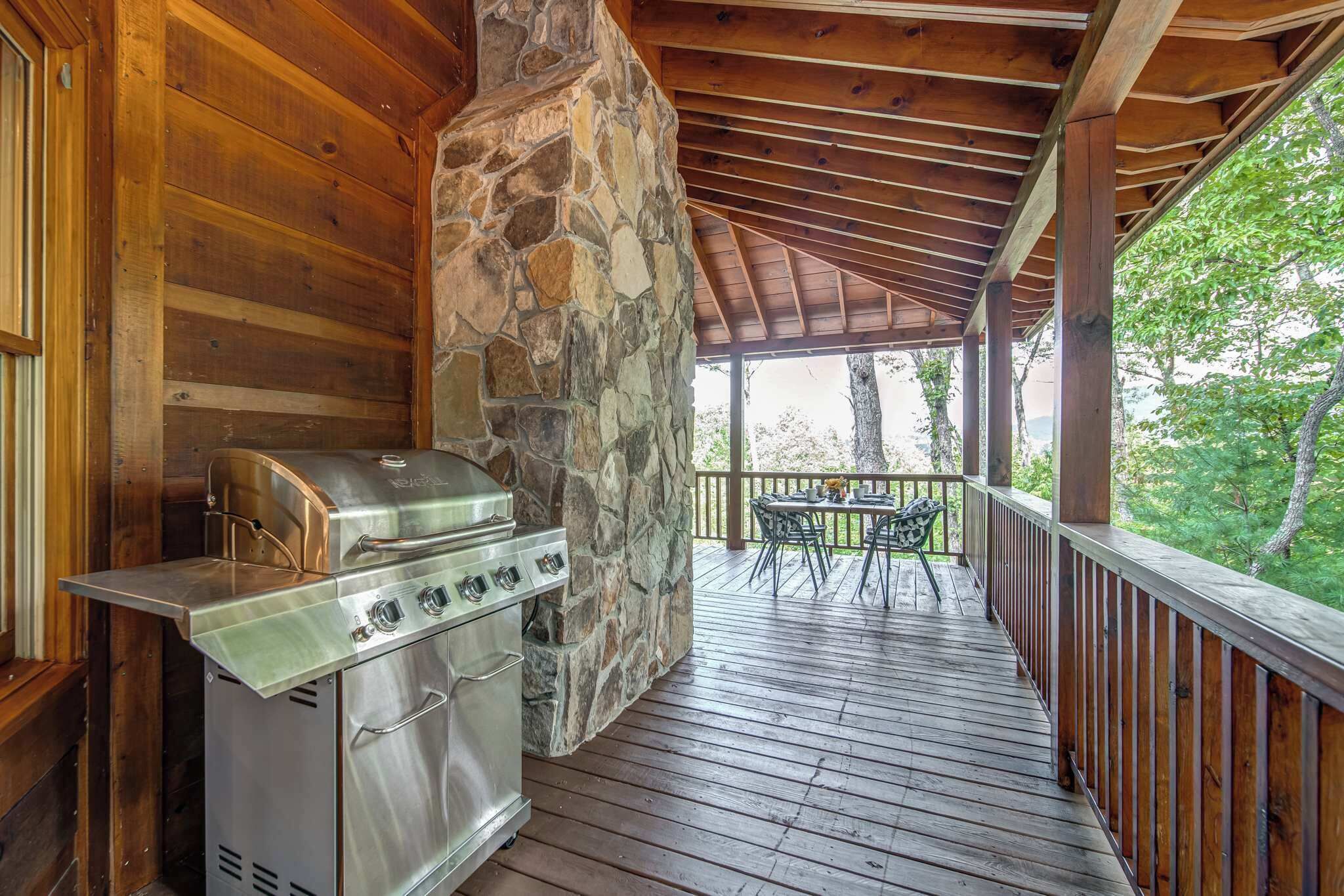 A covered outdoor area with a stone wall, a grill, and a table with chairs.