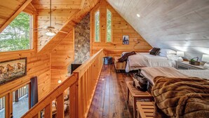 Una cabaña acogedora con habitación en altillo, pisos de madera, pared de piedra y un ventanal grande.