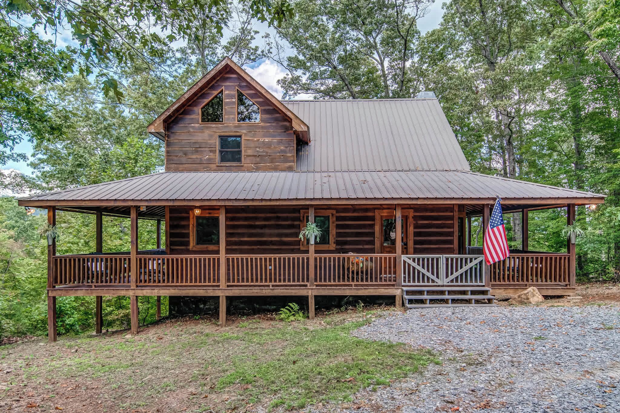 A rustic cabin with a metal roof, wooden deck, and an American flag.
