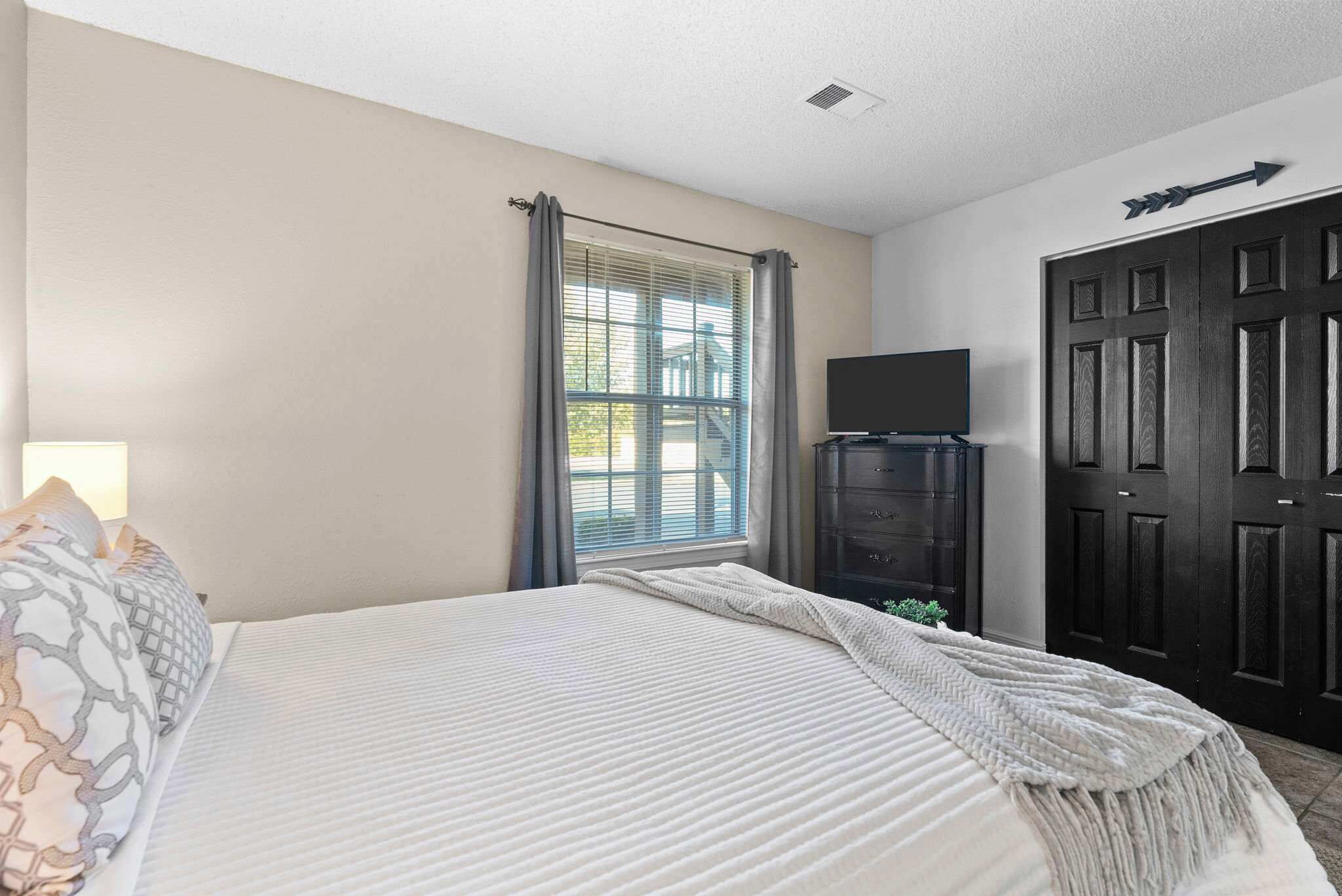 A bedroom with a bed, a TV, a wardrobe, and a window with curtains.