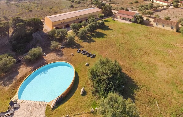 A large swimming pool surrounded by a grassy area with a few trees and a building in the background.