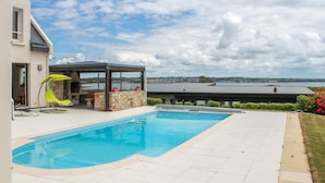 Une piscine avec un mur en pierre et un espace détente abrité.