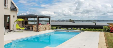 A swimming pool with a stone wall and a covered seating area.