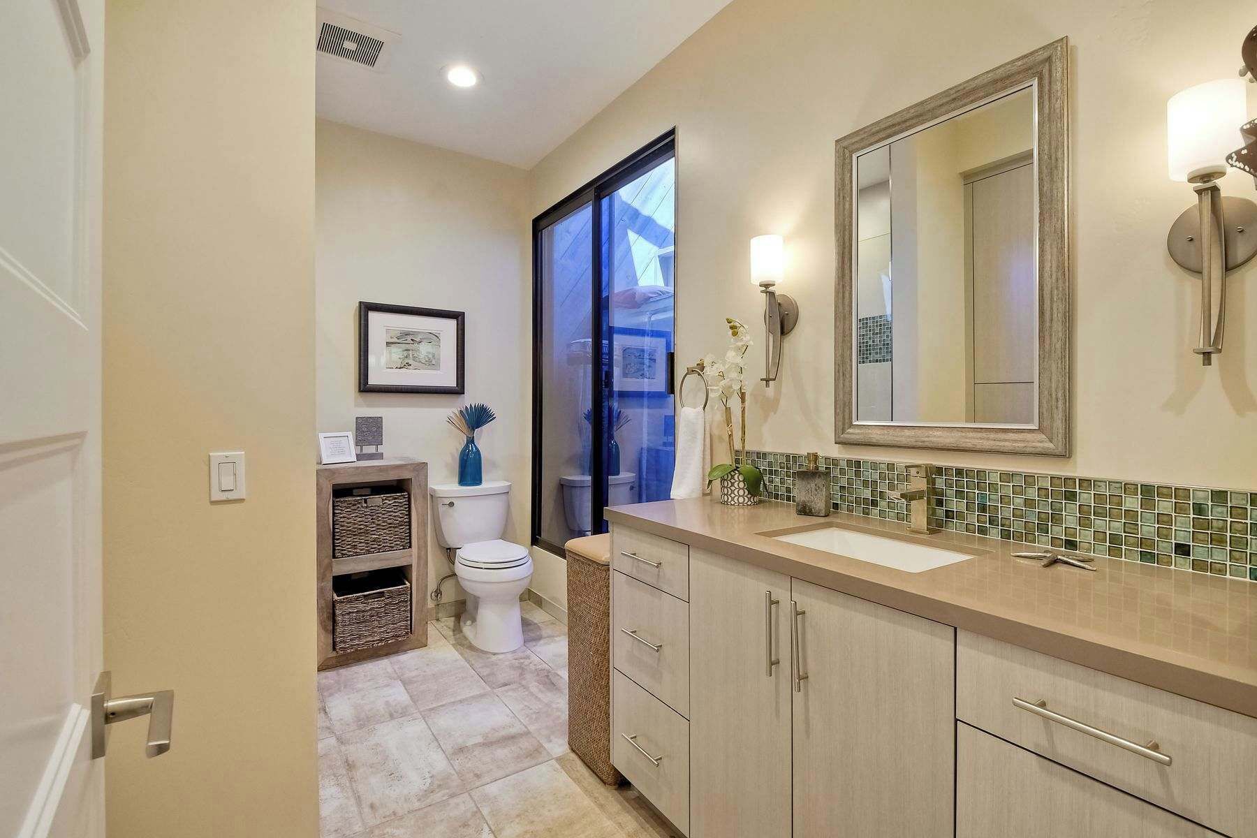 A bathroom with a toilet, a sink, and a mirror. There is a picture frame on the wall and a vase with flowers on the counter.