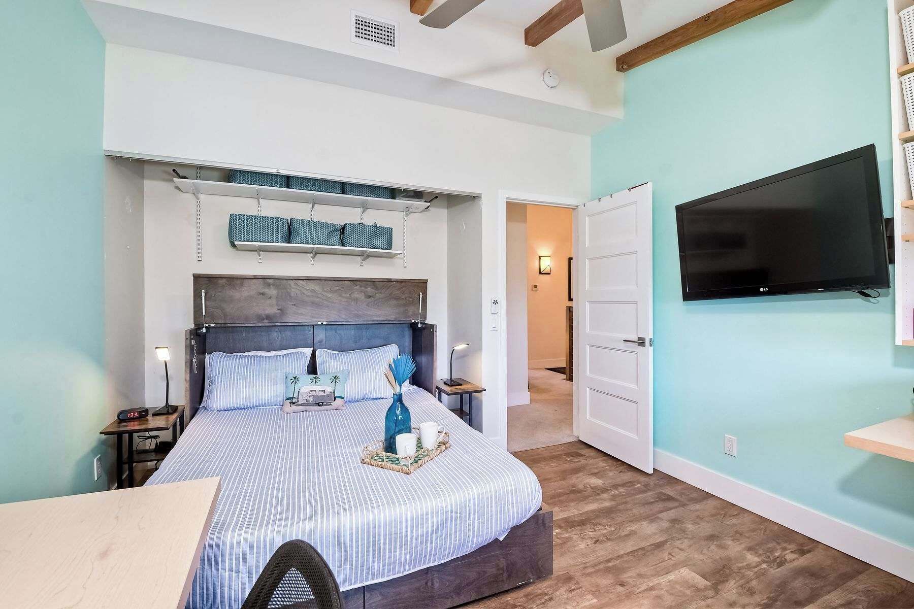 A bedroom with a bed, bedside tables, a TV, and a door leading to another room.