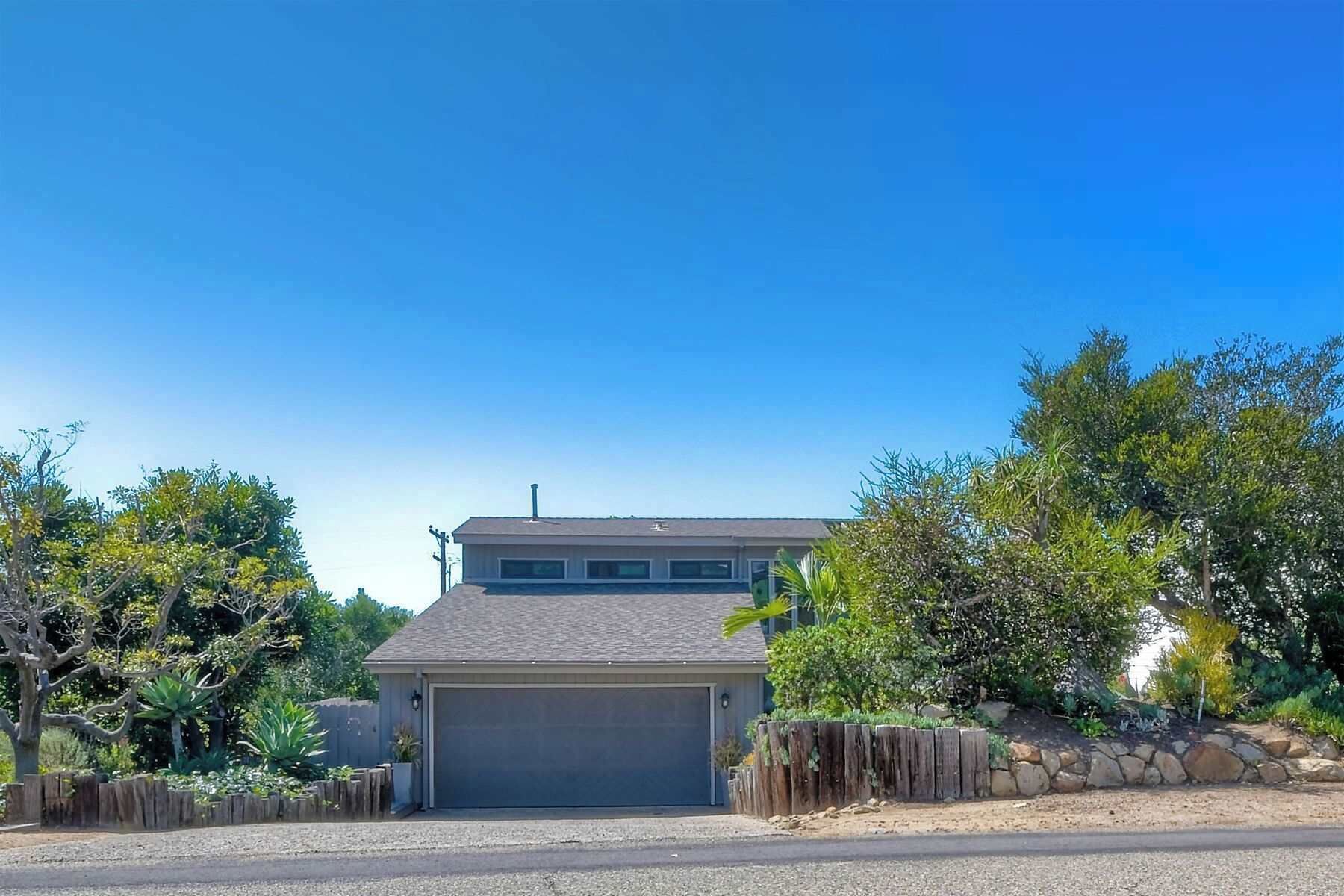 A single-story house with a garage, surrounded by a wooden fence and various plants.