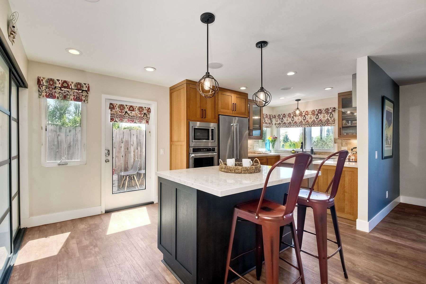 A modern kitchen with a central island, wooden cabinets, stainless steel appliances, and pendant lighting.