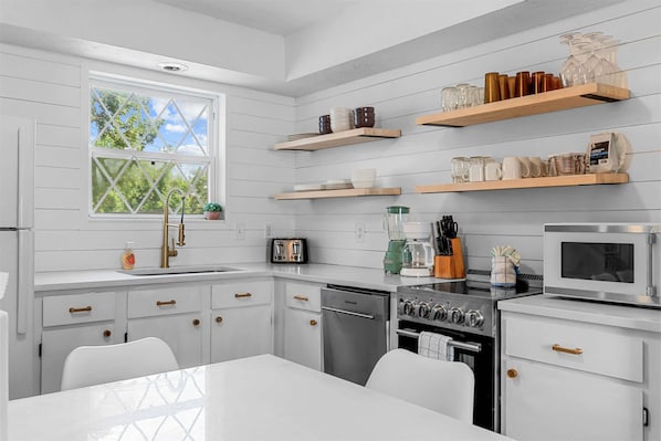 A modern kitchen with white cabinetry, a stainless steel refrigerator, a microwave, a stove, and a dishwasher. There are wooden shelves above the counter holding various kitchen items. - Tranquil Woods Retreat Branson (Branson)