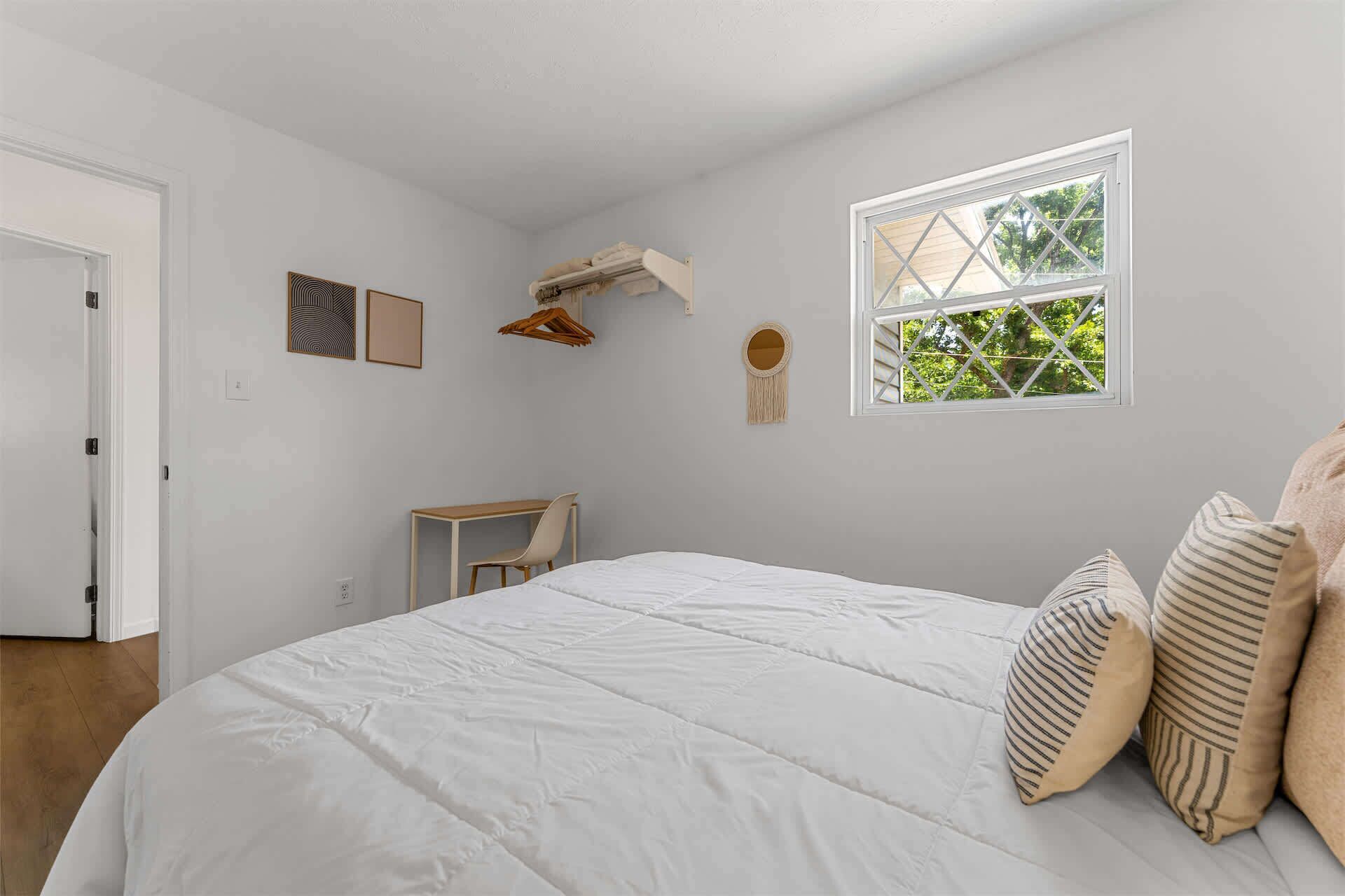 Une chambre à coucher avec un lit, un bureau, une chaise, une fenêtre et une porte.