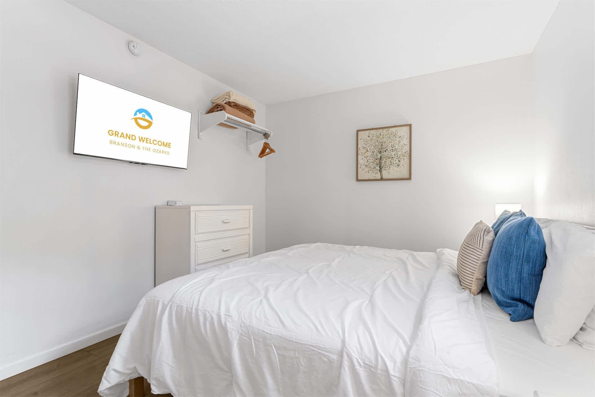 Une chambre à coucher comprenant un lit, une commode, une œuvre d’art accrochée au mur et une pancarte de bienvenue.