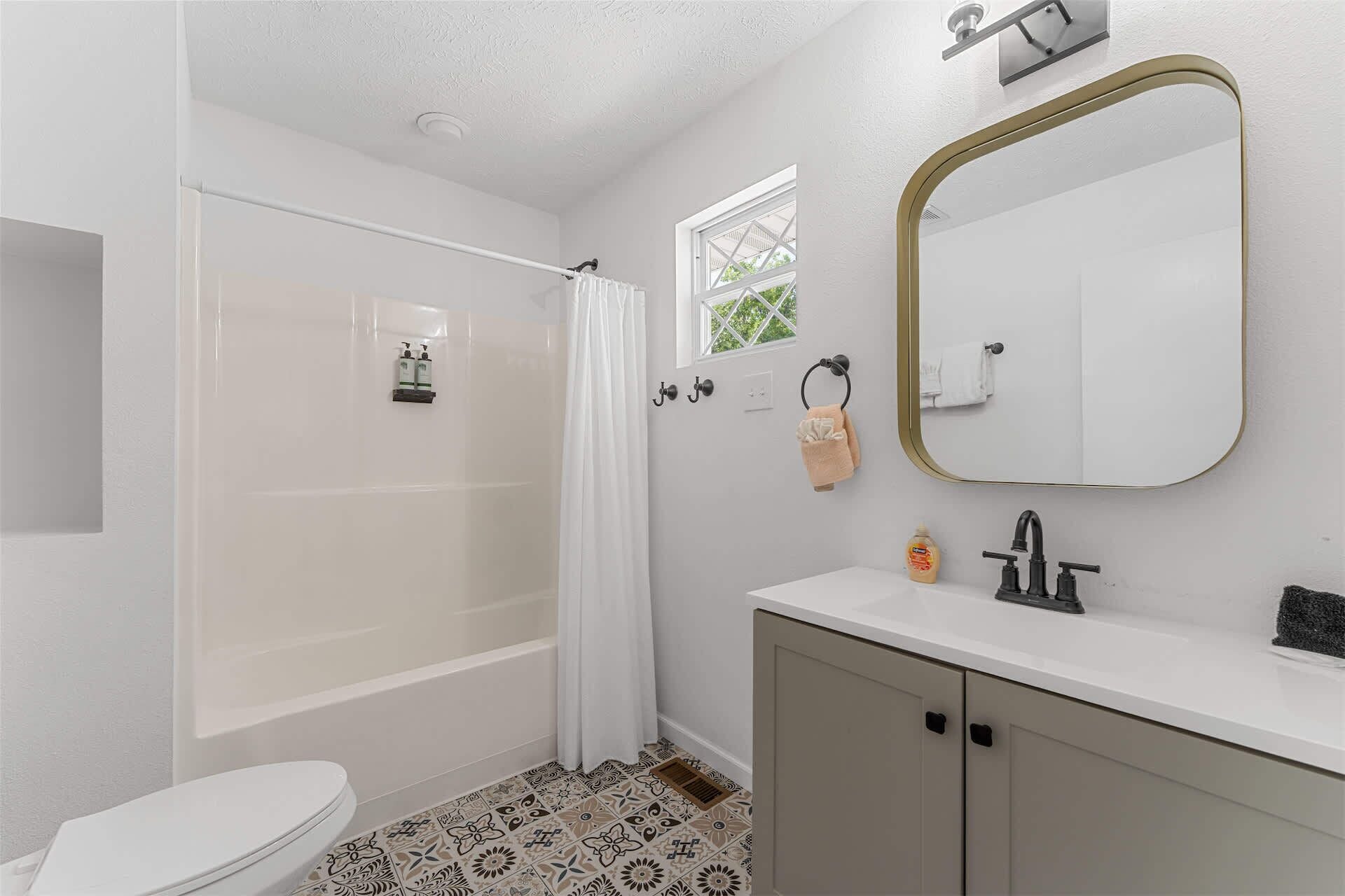 A bathroom with a shower, toilet, sink, and mirror.