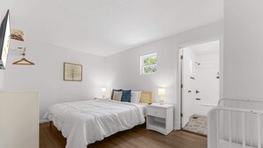 Une chambre à coucher comprenant un lit, des tables de chevet, une lampe suspendue, un tableau encadré et une porte donnant sur une salle de bain.