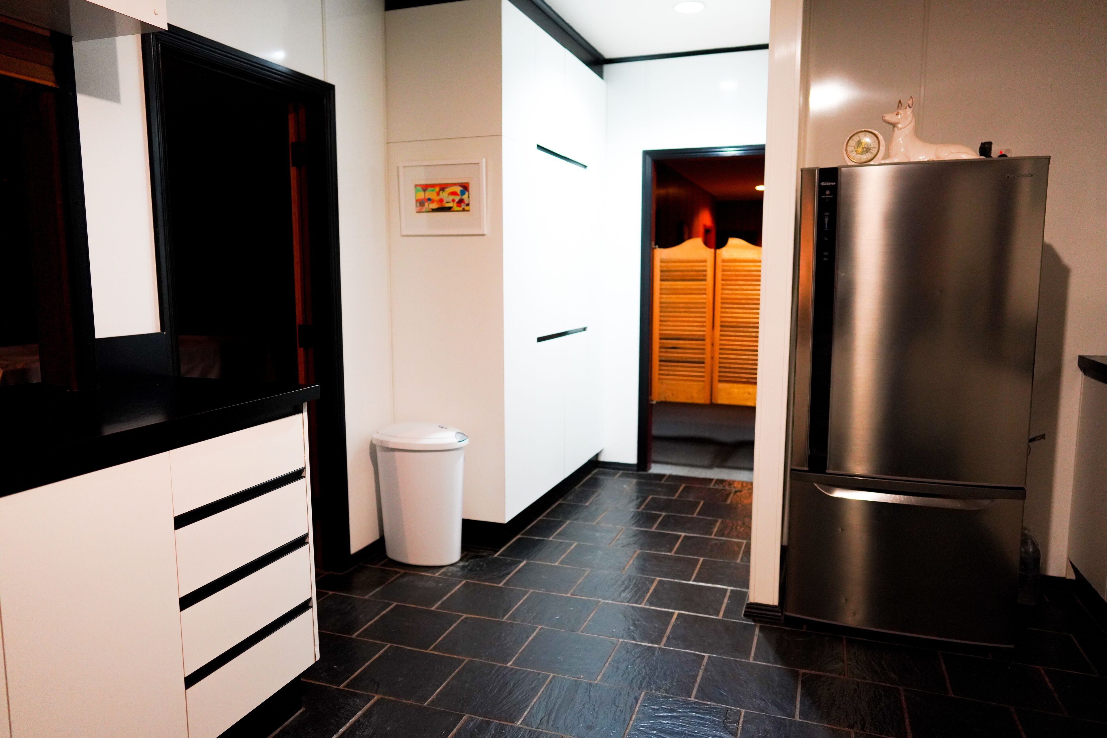 A modern kitchen with white cabinets, a stainless steel refrigerator, and a black tiled floor.
