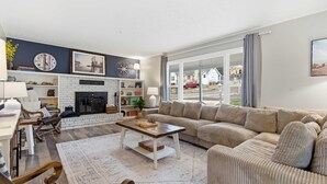 A living room with a fireplace, a sofa, a coffee table, and a view of the outside.