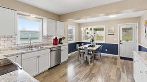 A modern kitchen with white cabinets, a granite countertop, a dishwasher, and a dining area with a table and chairs.