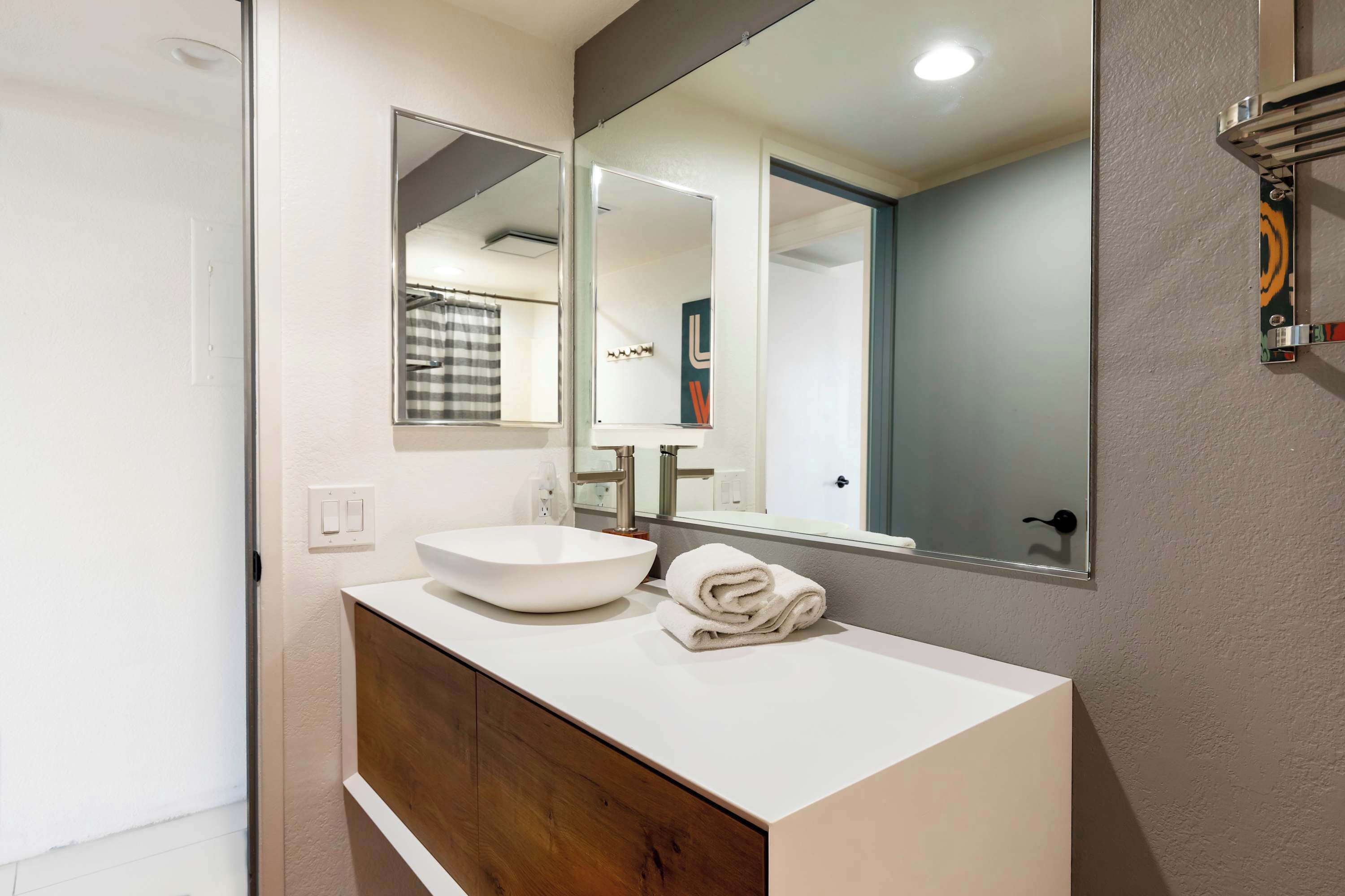 A modern bathroom with a white sink, a large mirror, and a wooden vanity.