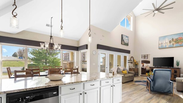 A spacious kitchen with a large island, white cabinetry, and a dishwasher. There is a dining area with chairs and a table, and a living room with a sofa and a TV. - Bchillin Retreat on Table Rock Lake (Hollister)