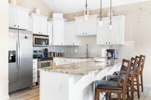 A modern kitchen with white cabinets, stainless steel appliances, a marble island, and wooden chairs.