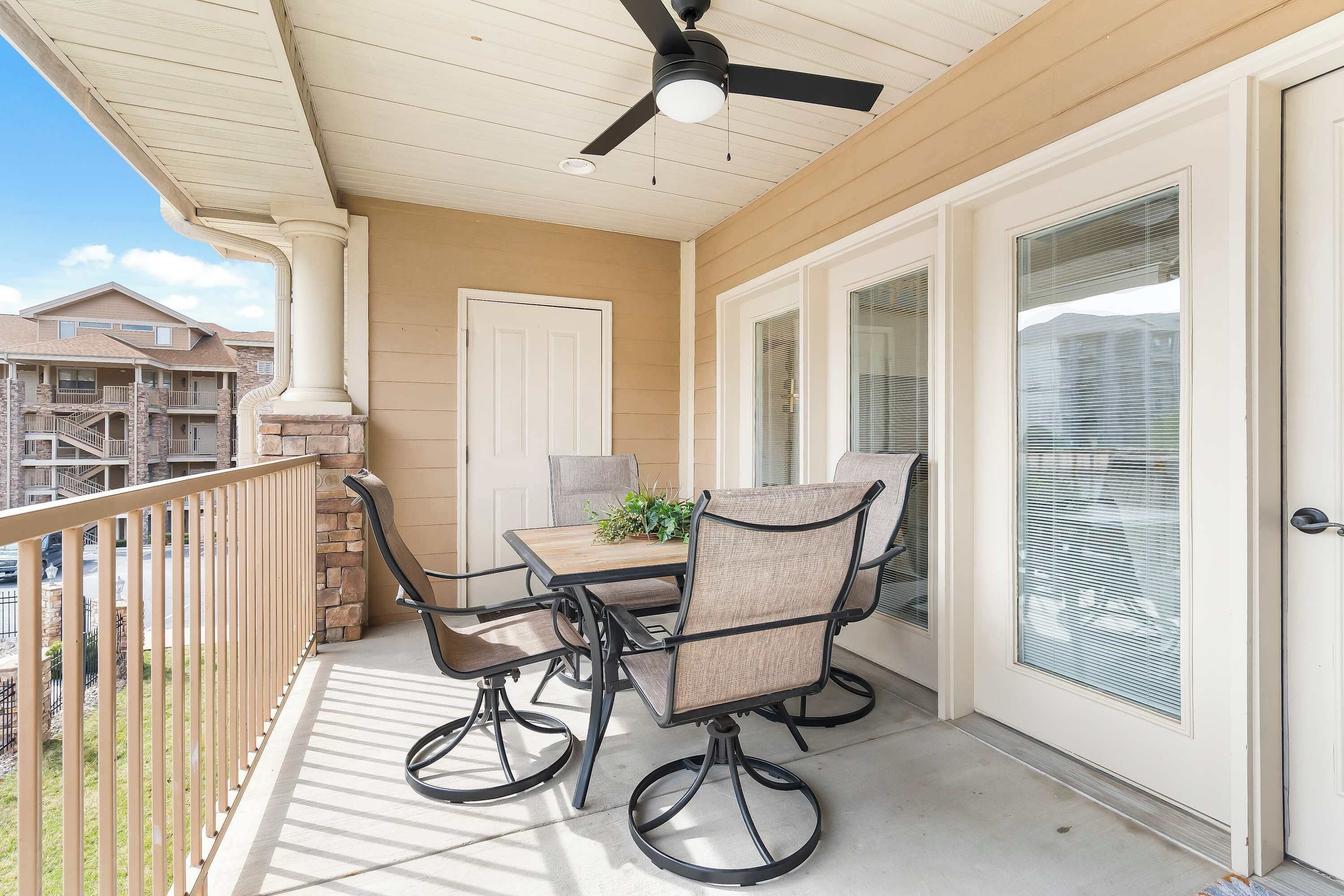 A covered patio area with a table and chairs, a ceiling fan, and a view of neighboring buildings.