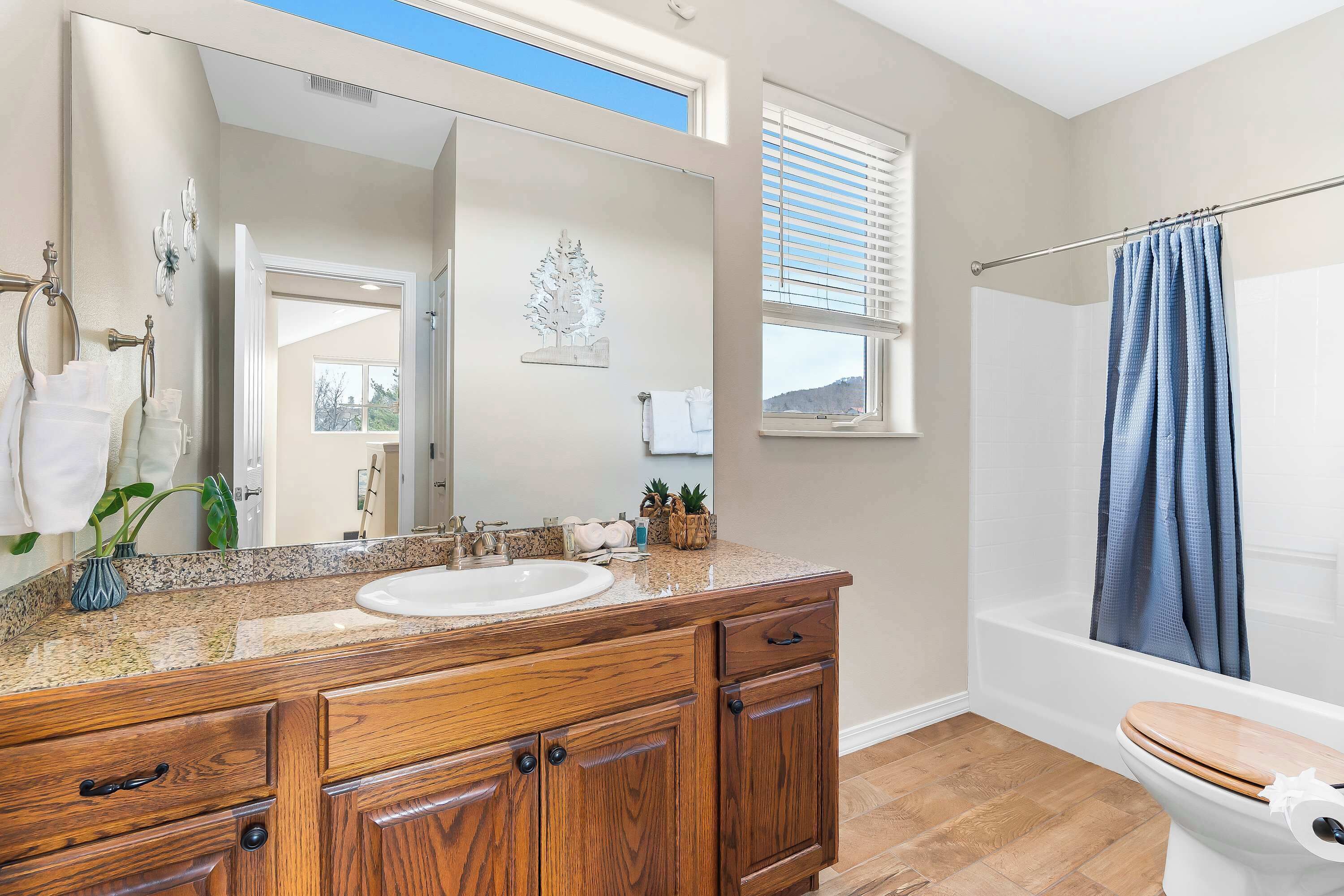 A bathroom with a wooden vanity, a large mirror, a white sink, and a shower with a blue curtain.