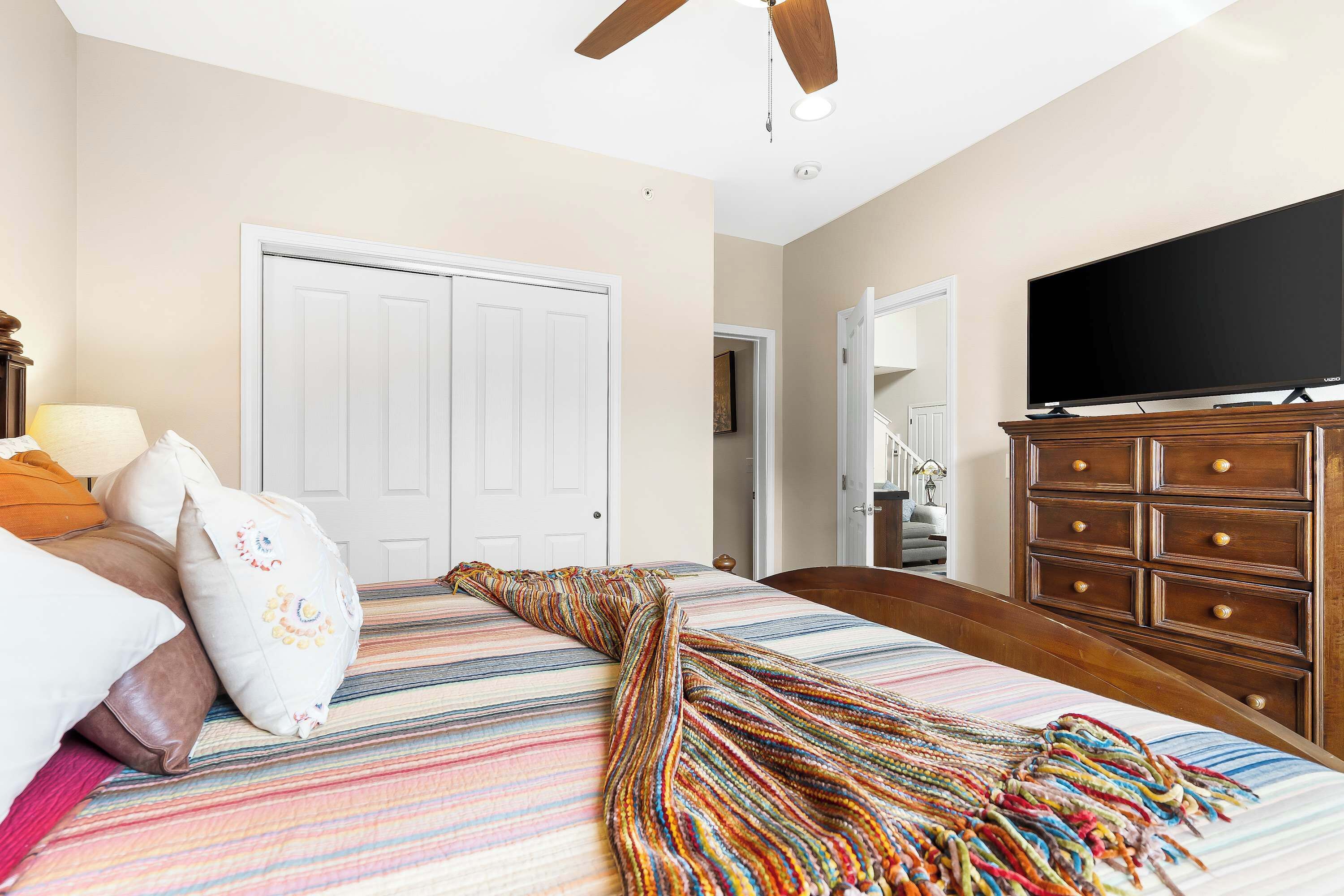 Un dormitorio con una cama, un televisor sobre una cómoda y una puerta que da a otra habitación.