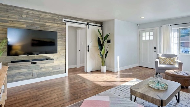 Un salón moderno con un televisor de pantalla plana montado en una pared de madera, una puerta corredera, una planta en maceta, un sofá y una mesa de centro.
