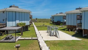A beachfront property with multiple cabins, a wooden deck, and a sandy pathway leading to a playground. - Resort Pool & Clear Ocean Views (Port Aransas)