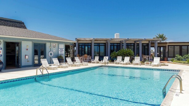 A swimming pool with lounge chairs and a building with large windows. - Resort Pool & Clear Ocean Views (Port Aransas)