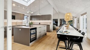 A modern kitchen with a central island, a dining area with a long table, and a large window providing natural light. - Awesome home in ålbæk with WiFi (Ålbæk)