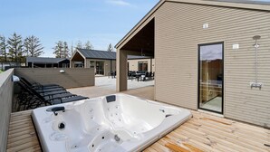A modern outdoor hot tub area with wooden decking, a covered seating area, and a building with large windows. - Awesome home in ålbæk with WiFi (Ålbæk)