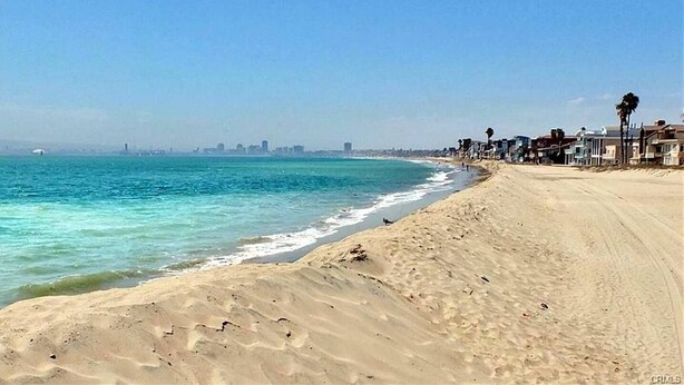 Una playa con vista despejada al océano y el horizonte de una ciudad a lo lejos.