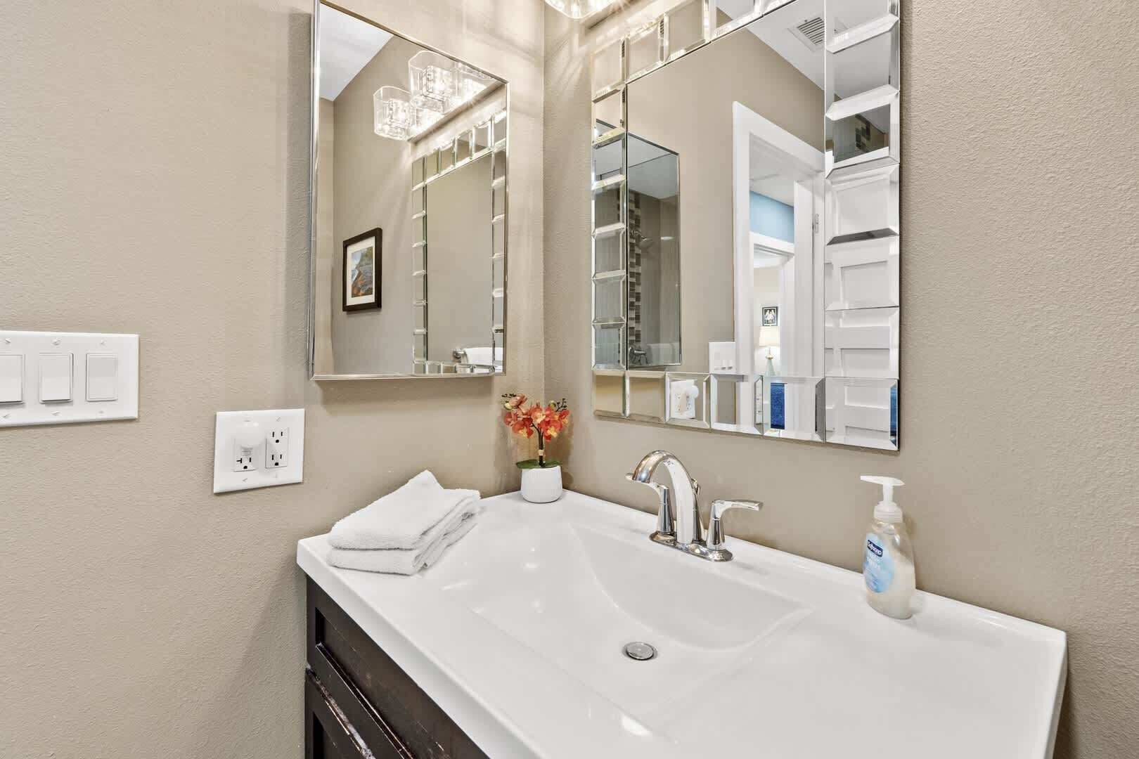 A bathroom with a large white sink, a mirror, a chandelier, and a small vase with flowers.