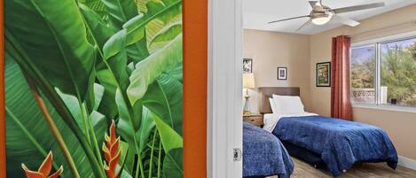 A hotel room with two beds, a ceiling fan, a window with a view, and a door with a tropical mural.