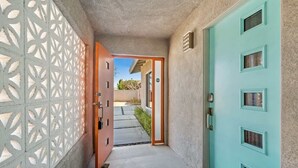 Un couloir avec une porte de couleur turquoise, un mur orné de motifs et un sol en béton.