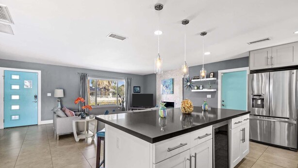 Une cuisine moderne dotée d’un grand îlot central, d’appareils électroménagers en acier inoxydable et de luminaires suspendus.