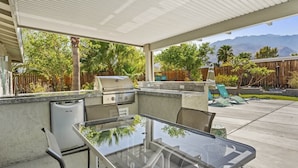 Une terrasse extérieure avec une table en verre, un barbecue et un lave-vaisselle encastré.