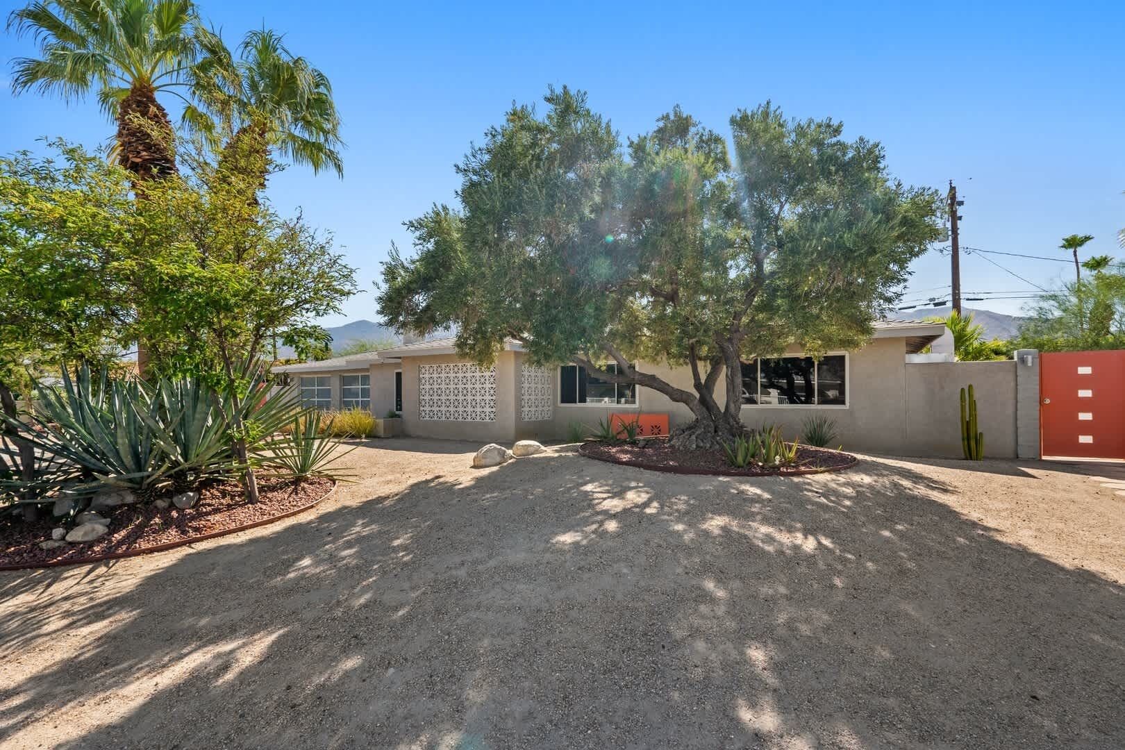 A residential property with a gravel driveway, a palm tree, and a red gate.