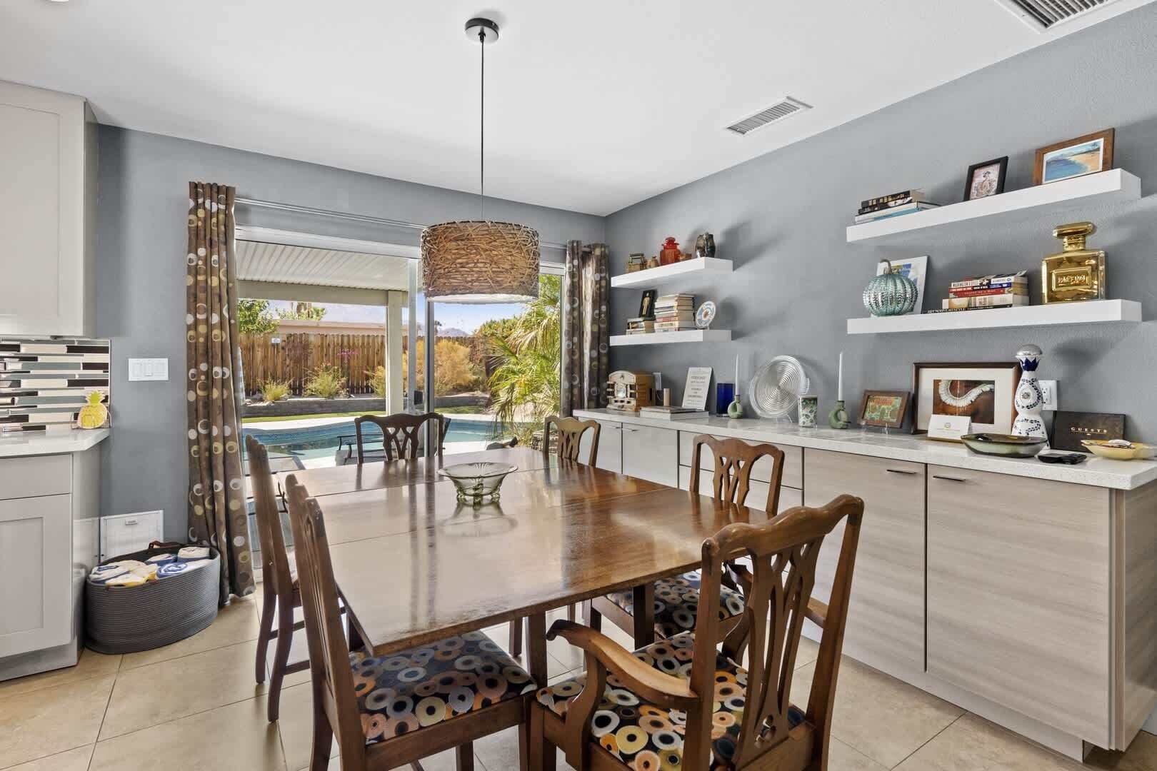 A modern kitchen with a dining area, a pool view, and decorative shelves.
