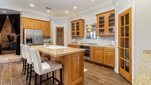 A modern kitchen with wooden cabinets, a central island with bar stools, stainless steel appliances, and a brick accent wall.