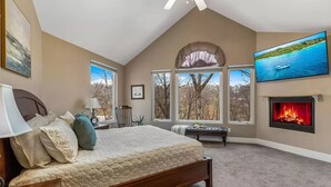 A bedroom with a large bed, a fireplace, and a TV mounted on the wall.
