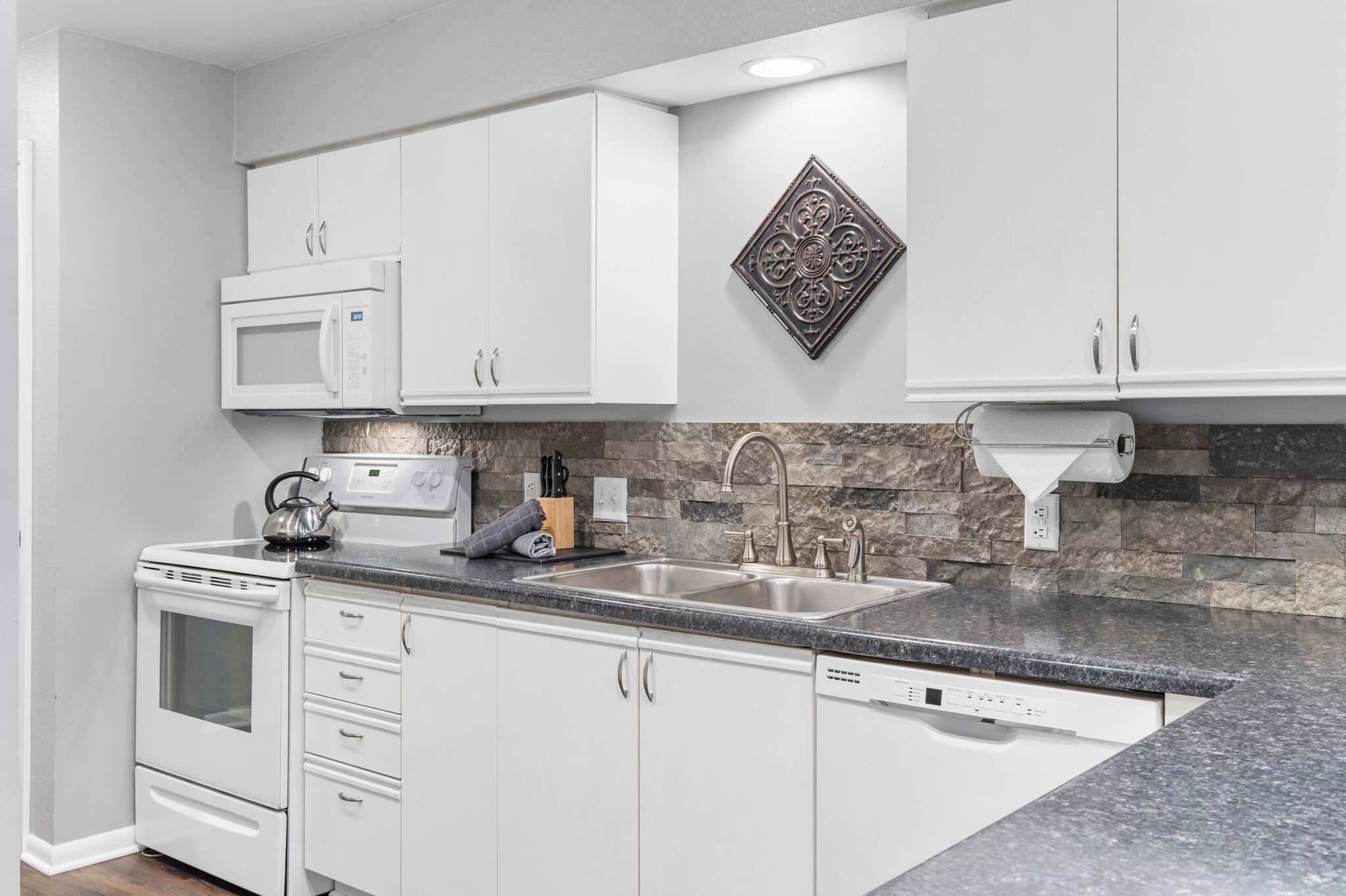 Une cuisine moderne avec des meubles blancs, un plan de travail en granit, un four à micro-ondes, une cuisinière et un évier.
