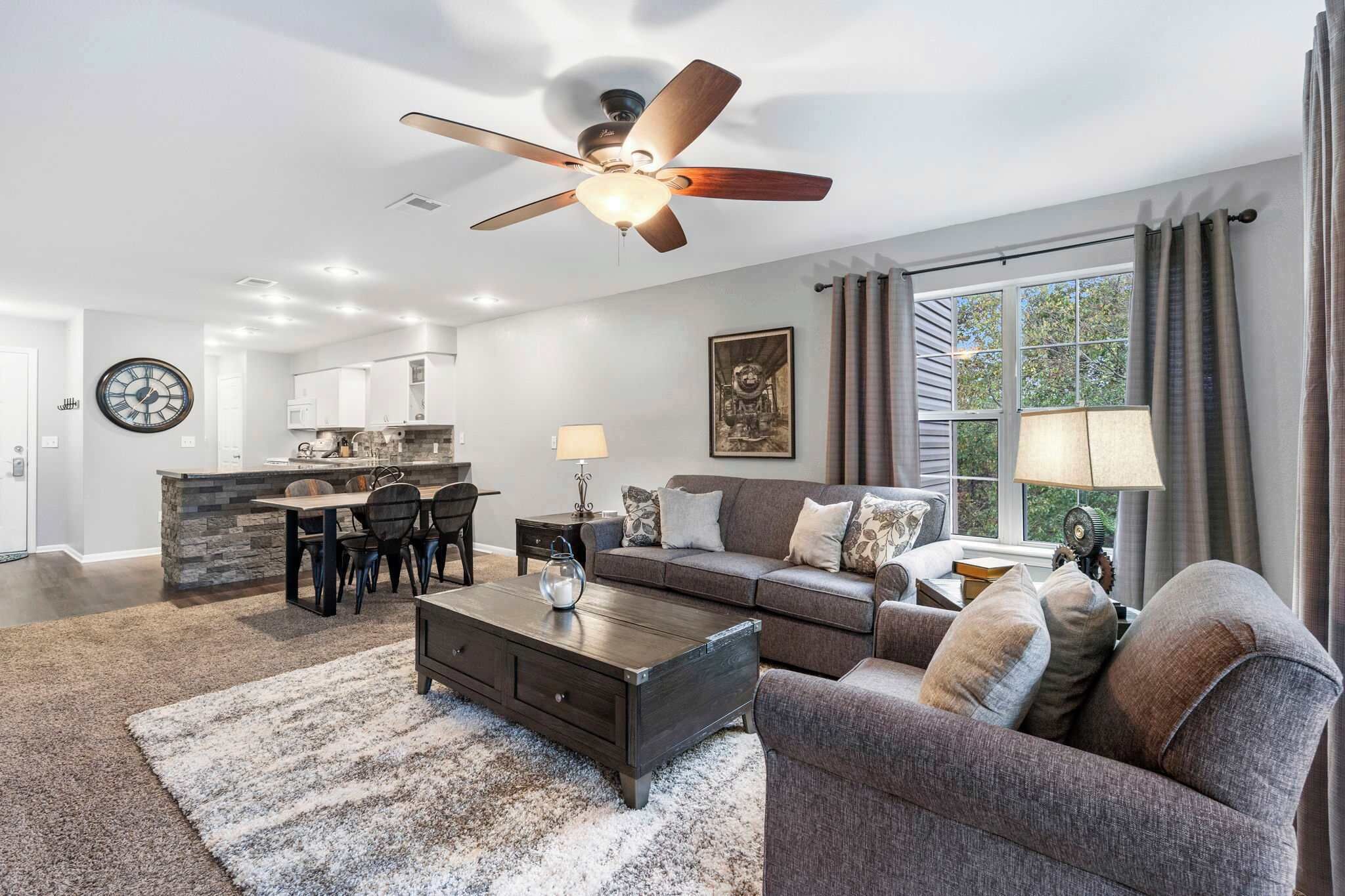 A spacious living room with a dark wooden coffee table, a gray sofa, and a dining area with a stone island and chairs.