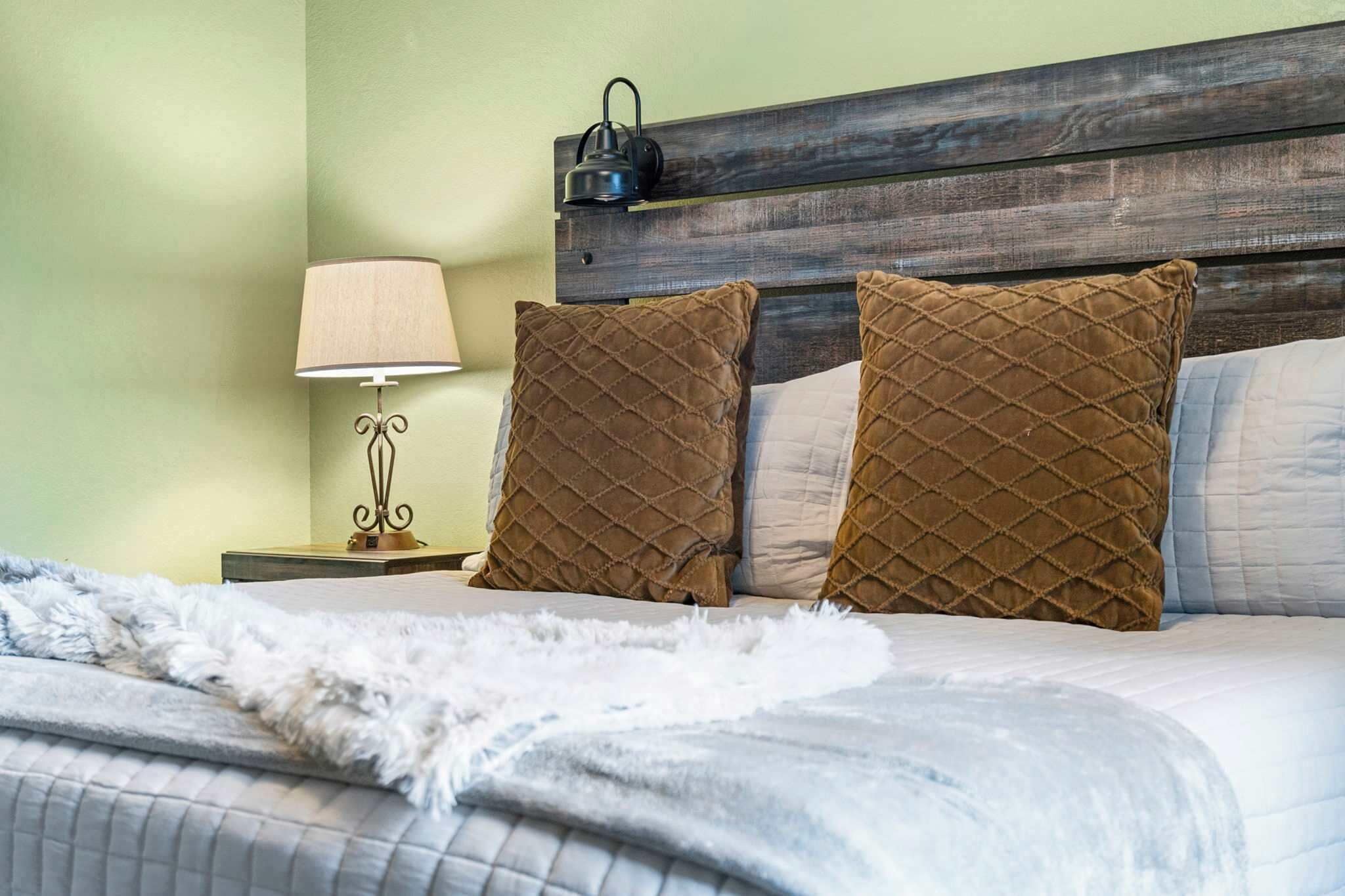Cama bem arrumada com duas almofadas castanhas, um cobertor branco e cabeceira de madeira.