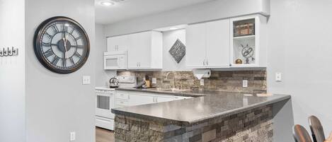 A modern kitchen with a central island, white cabinetry, and a large wall clock.
