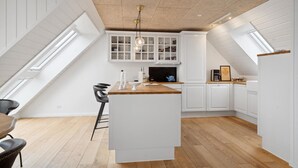 Una cocina moderna con armarios blancos, encimera de madera y una isla central. Hay dos sillas negras y un hervidor azul sobre la isla.